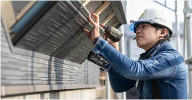 白いヘルメットを着用した職人が建物の外壁工事を行っている様子