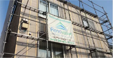 足場が組まれた建物にリノベーション工事の看板が掲示されている現場