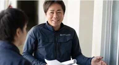 紺色の作業着を着た担当者が顧客と笑顔で打ち合わせをしている様子